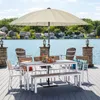 An outdoor dining set with a table, chairs, and bench is set up on a wooden deck overlooking a lake with houses in the background. Anteprima dell’immagine prodotto