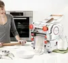 A woman is in a kitchen making pasta with a pasta machine. Produktbild-Vorschau
