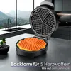 A heart-shaped waffle maker is shown in a modern kitchen setting, with freshly made waffles on the plate and the waffle maker open. Náhled obrázku produktu