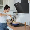 A woman is cooking in a modern kitchen with a black range hood. Voir les images du produit