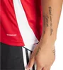 A close-up of a person wearing a red and white Adidas shirt and black and white striped shorts. Anteprima dell’immagine prodotto