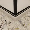 A close-up view of the corner of a shower enclosure, showing the black frame and the white base against a terrazzo-style floor. Produktbild-Vorschau