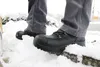 A person wearing black work boots and gray pants stands in the snow, with a shovel visible on the left. Produktbild-Vorschau