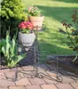 A metal plant stand with three tiers holding potted flowers on a brick patio. Náhľad obrázku produktu
