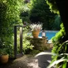 A modern outdoor lamp illuminates a garden path next to a swimming pool. Anteprima dell’immagine prodotto