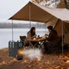 A couple is eating at a table under a canopy tent by a lake, with a diesel heater in the foreground. Voir les images du produit