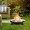 A fire pit with burning logs sits on a grassy lawn in a backyard setting, with outdoor furniture and greenery in the background. Anteprima dell’immagine prodotto