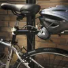 A bicycle helmet and lock are attached to a bicycle seat post, with a brick wall in the background. Podgląd zdjęcia produktu