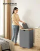 A woman is putting clothes into a two-compartment laundry basket in a bedroom. Produktbild-Vorschau