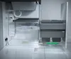 A cutaway view of a kitchen cabinet showing a sink, plumbing, and a pull-out trash bin system. Produktbild-Vorschau