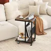 A C-shaped side table with a laptop, coffee cup, books, and headphones on it, placed next to a sofa. Voir les images du produit
