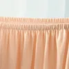 A close-up view of the top elasticated edge of a beige fabric product, likely a stool cover or cushion cover, with a blurred background of light blue and white stripes. Produktbild-Vorschau
