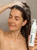 A woman is washing her hair in a shower, holding a bottle of shampoo. Produktbild-Vorschau