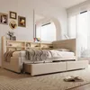 A bedroom scene featuring a beige upholstered bed with a built-in bookshelf headboard and a pull-out trundle bed. The room has white sheer curtains and framed pictures on the wall. Produktbild-Vorschau