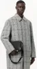A man wearing a plaid coat holds a black bag. Voir les images du produit
