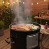 A barbecue grill with food cooking on it, set up on a wooden deck at dusk, with string lights overhead. Produktbild-Vorschau