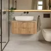 A modern bathroom with a wooden vanity, a white vessel sink, and a wall-mounted toilet. Voir les images du produit