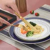 A person is using gold cutlery to eat a meal of pasta, shrimp, and broccoli from a decorative plate. Anteprima dell’immagine prodotto