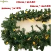 A close-up view of a green artificial Christmas garland with small yellow LED lights woven throughout, displayed against a white background. Produktbild-Vorschau