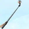 A hand holding a black selfie stick extended with a smartphone attached, against a light blue sky background. Náhled obrázku produktu