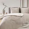 A neatly made bed with taupe bedding and pillows, set against a neutral background. Voir les images du produit