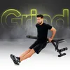 A man is performing a dip exercise on a black weight bench. The word "Grind" is displayed in large, glowing yellow letters in the background. Produktbild-Vorschau