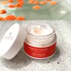 A jar of face cream with its lid off, placed on a textured surface with a blurred background of orange objects in water. Produktbild-Vorschau
