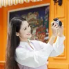 A woman is taking a selfie with a camera in front of a colorful mural. Podgląd zdjęcia produktu