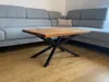 A coffee table with a black metal spider base and a wooden top is placed in front of a gray sectional sofa in a living room. Anteprima dell’immagine prodotto