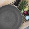 A frying pan is placed on a wooden board next to some ingredients and a cooling rack. Produktbild-Vorschau