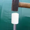 A hammer is poised to strike a white cylindrical object, which is mounted on a metal pole. The background is a textured green surface. Voir les images du produit