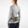 A person wearing a grey long-sleeved shirt and dark blue pants, with a green fanny pack around their waist. Voir les images du produit