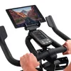 Close-up of a person's hands on the handlebars of a Schwinn indoor cycling bike, with a tablet mounted above the console. Produktbild-Vorschau