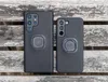 Two black phone cases with Quad Lock mounts are shown on a weathered wooden surface. Produktbild-Vorschau