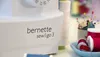 Close-up of a white sewing machine with the brand name 'bernette sew&go 3' visible, alongside spools of thread and pins in the background. Produktbild-Vorschau