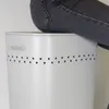 A person's legs are visible sitting on top of a light gray laundry basket. Produktbild-Vorschau