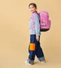 A young girl wearing a pink backpack and jeans walks against a plain yellow background. Voir les images du produit