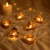 A string of heart-shaped LED lights and a candle on a textured surface. Produktbild-Vorschau