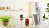 A kitchen counter with a SodaStream machine, a bottle of Pepsi syrup, a glass of cola, and a potted plant. Náhľad obrázku produktu
