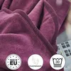 A close-up of a folded dark violet blanket with informational icons in the bottom corners. Produktbild-Vorschau