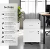 A white roll container with two drawers is shown in an office setting next to a desk and a plant. Náhled obrázku produktu