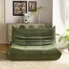 A green sofa is placed in a living room setting, with a cabinet and artwork in the background. Produktbild-Vorschau