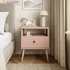 A pink nightstand with a drawer and an open shelf, decorated with a lamp, candle, and a small decorative item. Náhled obrázku produktu