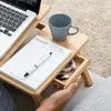 A person is using a portable laptop table with a laptop, notebook, pen, and mug on it. Produktbild-Vorschau