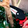 A hand is holding a red and black mini chainsaw and cutting a tree branch. Náhled obrázku produktu
