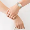 A close-up shot of a person's wrists, one wearing a silver and gold Citizen watch. Voir les images du produit