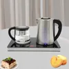 A glass teapot and a stainless steel kettle are placed on an induction heating base, with a slice of cake and cookies in the foreground. Podgląd zdjęcia produktu
