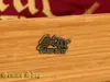 A close-up of a wooden box with a metal emblem and text on the bottom left. Anteprima dell’immagine prodotto
