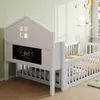 A white children's bed with a house-shaped headboard and a chalkboard panel is shown in a room with light green walls and wooden flooring. Náhľad obrázku produktu