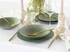A table setting with green stoneware plates, bowls, and gold cutlery, along with glassware and decorative elements. Náhľad obrázku produktu